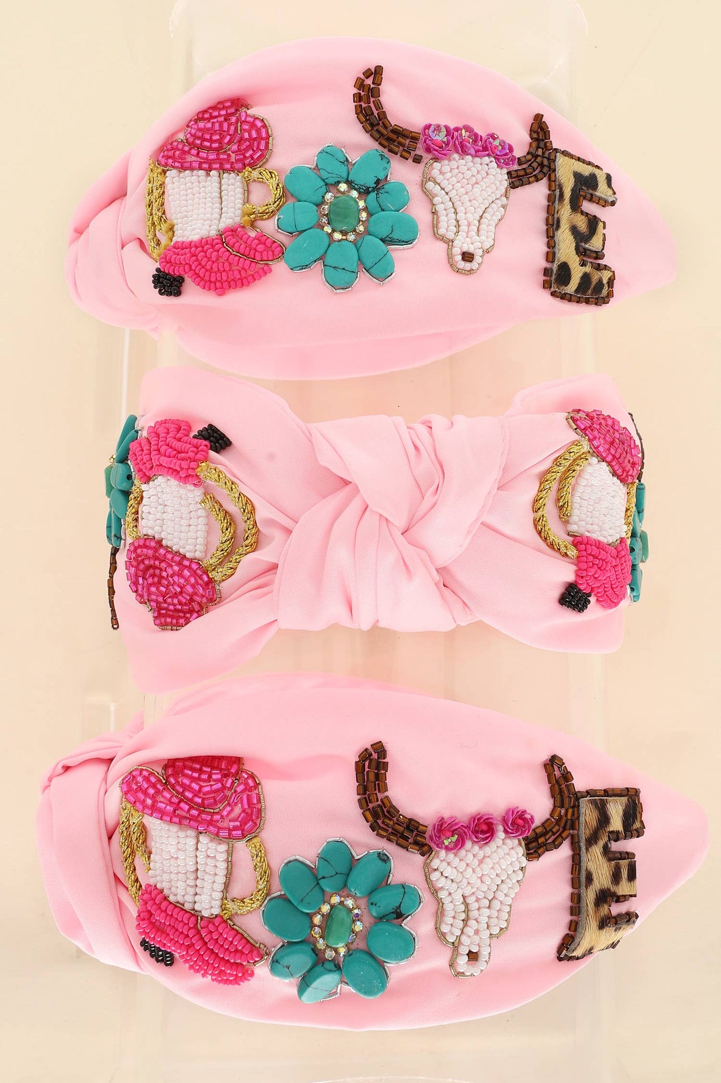 A  knotted headband in pink, featuring beaded cowboy hats, turquoise flowers, steer skulls, and rhinestone embellishments.