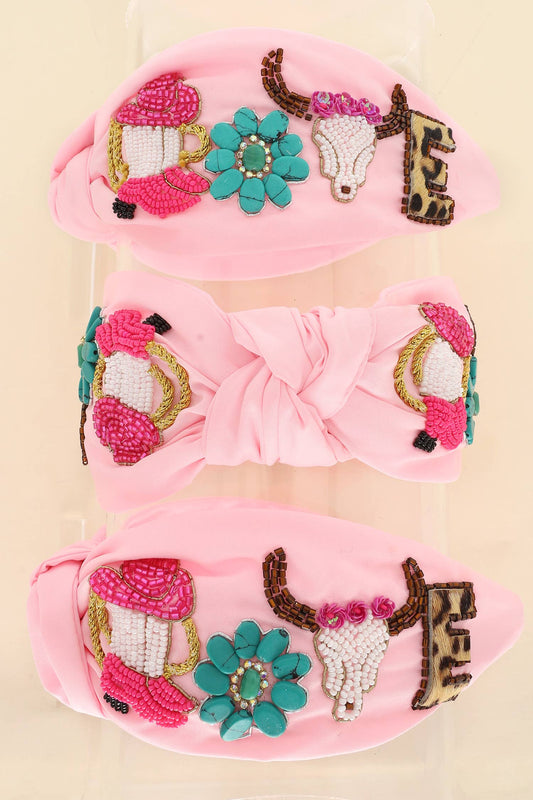 A  knotted headband in pink, featuring beaded cowboy hats, turquoise flowers, steer skulls, and rhinestone embellishments.