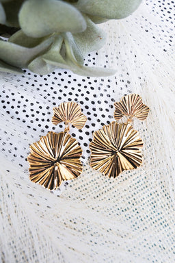 A pair of gold-toned statement earrings featuring a textured, floral-inspired design with a double-drop silhouette. The intricate ridged detailing catches the light for an elegant yet bold look. Perfect for adding a touch of sophistication to any outfit, from casual denim to evening wear.